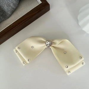 Close-up of cream satin bow hair clip with a central heart rhinestone and crystal beads