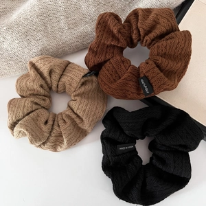 Close-up of three knitted cable knit scrunchies in coffee, khaki, and black colors