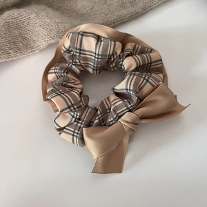 Detail of warm brown plaid scrunchie with satin bow on a cozy aesthetic background
