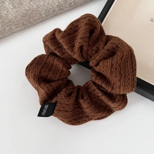 Detailed macro view of coffee-colored knitted scrunchie with cable texture and fabric label