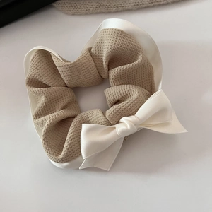 Detailed view of checkered scrunchie with large satin bow in warm khaki and cream