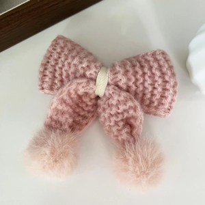 Dettaglio di fermaglio per capelli a fiocco rosa in maglia con pompon morbidi e accento crema