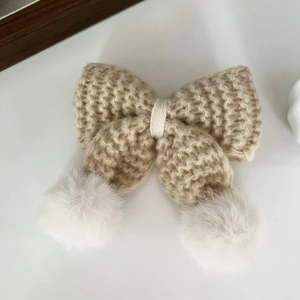 Dettaglio del fermaglio per capelli in maglia color crema con pompon bianchi soffici