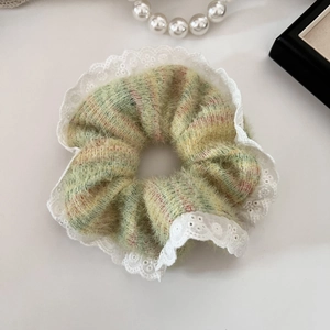 Dettaglio di scrunchie verde soffice con bordi in pizzo bianco su uno sfondo crema
