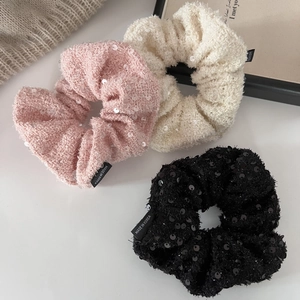 Three sequined tweed scrunchies in pink, beige, and black on a minimalist white background