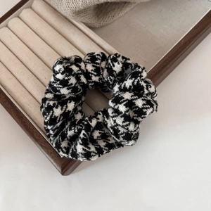 Close-up of black and white houndstooth hair scrunchie on a premium beige velvet tray