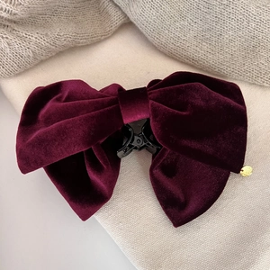 Detail of burgundy velvet bow hair claw clip with golden pendant and soft texture