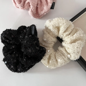 Close-up of glitter sequins on tweed scrunchies in pink, black, and beige colors