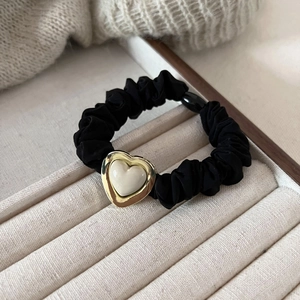 Detail of black scrunchie with heart metal charm on beige velvet jewelry tray