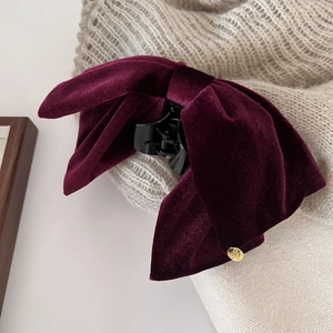 Detail of burgundy velvet bow hair claw clip with golden metal charm on knit background
