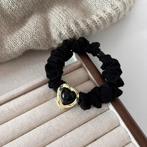 Detailed close-up of a black scrunchie with a gold-trimmed heart on a soft knit fabric