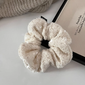 Close-up of beige tweed scrunchie with sequins and black woven label on soft background