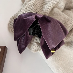 Detailed shot of purple velvet bow hair claw clip with golden metal tag on knit background