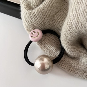 Détail du smiley en résine rose et de la perle dorée sur un élastique noir à cheveux