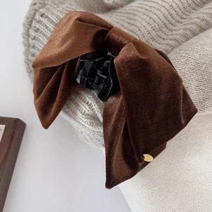 Detail of brown velvet bow hair claw clip with golden metal tag on beige knit sweater