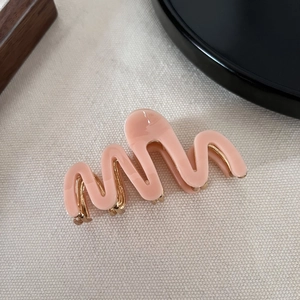 Detailed view of wave-shaped pink acetate hair claw clip with golden metal teeth