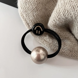 Détail de l'élastique à cheveux avec pendentif smiley noir et perle dorée champagne