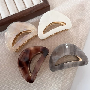 Detail of four acetate hair claws in tortoise shell and marble patterns with gold metal teeth