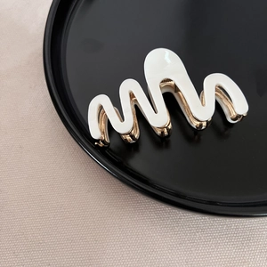 Detail of wavy acetate hair claw clip with golden metal base and smooth cream finish