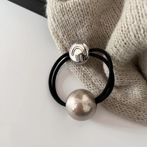 Détail d'un élastique à cheveux noir avec perle et pendentif métallique en forme de sourire
