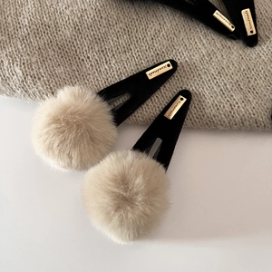 Cute plush pom-pom hair clip with golden metal handmade tag on knitted background