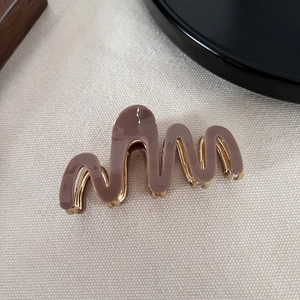 Detail of coffee brown wavy acetate hair claw with golden metal base on beige fabric