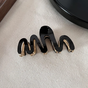 Detail of wavy black hair claw clip with golden metal teeth on white textured fabric