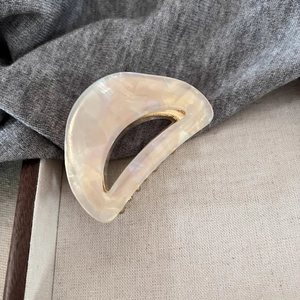 Detailed shot of cream acetate hair claw with pearlescent finish and golden metal frame