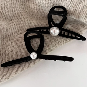 Detailed view of large black velvet hair claw and pin with pearl accent on beige knit