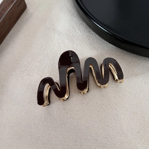 Close-up of wave-shaped hair claw clip in dark coffee acetate with golden metal frame