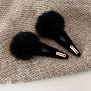 Detail of plush black pompom hair clips with gold handmade tags on knit background