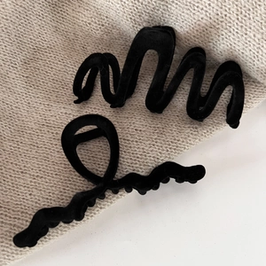 Detail of two black velvet hair claws in wave and twist shapes on beige knit background