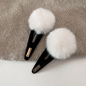 Detailed close-up of sweet plush pompom hair clips with gold handmade metal label