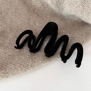 Close-up of black velvet wave hair claw clip with flocking texture on knit background