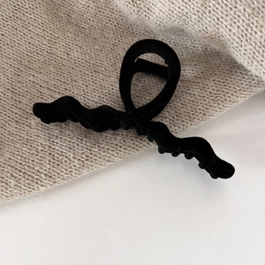 Close-up of black velvet hair claw clip with elegant wave design on knit background