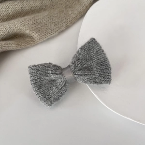 Detail of grey knitted bow hair clip showing soft texture and silky center ribbon