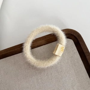 Détail d'un chouchou en peluche blanc cassé avec un bouton fleur jaune sur plateau bois