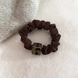 Close-up of a dark brown satin leopard print scrunchie with acrylic tortoiseshell bead