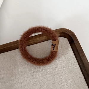 Détail d'un chouchou en peluche marron avec étiquette papillon sur plateau bois