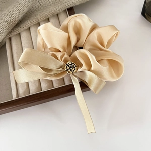Gros plan sur chouchou en satin champagne avec nœud en ruban et boucle rose en métal