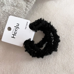 Close-up of black fuzzy plush hair scrunchie with Henju brand tag on textured fabric