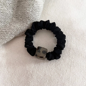 Detail of leopard print resin bead on black elastic hair scrunchie against neutral fabric