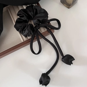 Detail view of a black satin hair scrunchie with elegant tulip ribbon on a wooden box
