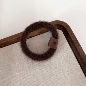 Gros plan sur un chouchou en peluche marron café avec une étiquette logo en cuir