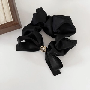 Détail d'un chouchou en satin noir avec nœud et boucle de rose dorée sur fond blanc