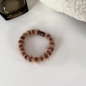 Detail view of a fluffy dark brown plush hair scrunchie with a glossy resin buckle