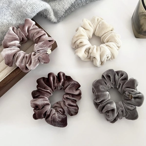 Close-up of four soft velvet hair scrunchies with silver charms on a wooden tray