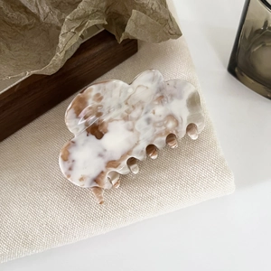 Close-up of marbled acetate hair claw clip on beige fabric with minimalist decor