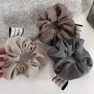 Detailed view of three-piece tweed scrunchies with herringbone pattern and side labels