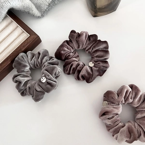 Three-piece velvet scrunchie set in grey and brown tones with metallic logo charms